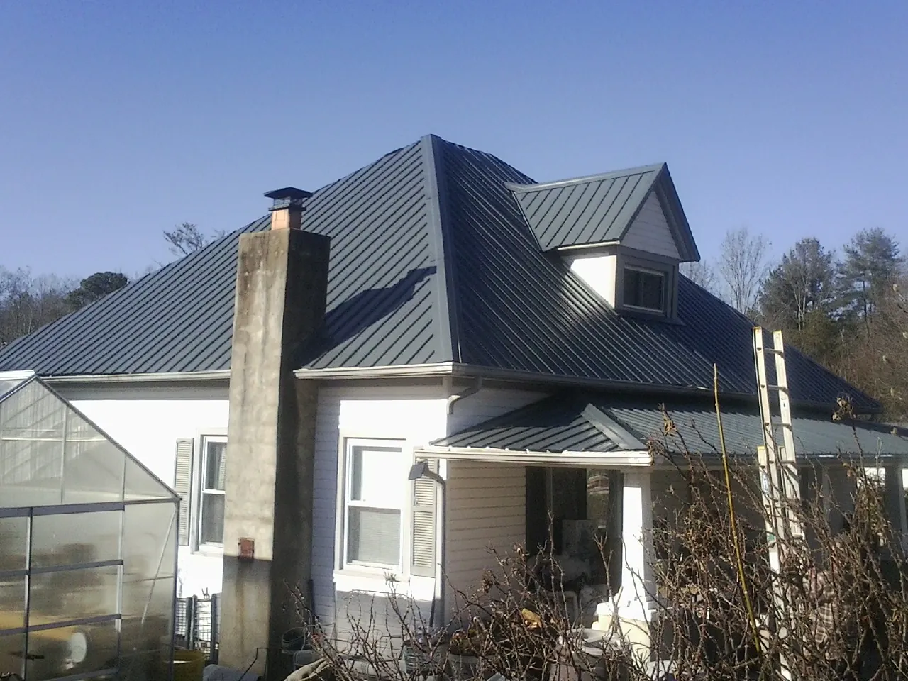 Dark blue standing seam metal roof on a white farmhouse with dormer — Slate & Tile Roof Repair by Roofing Brothers in Dallas