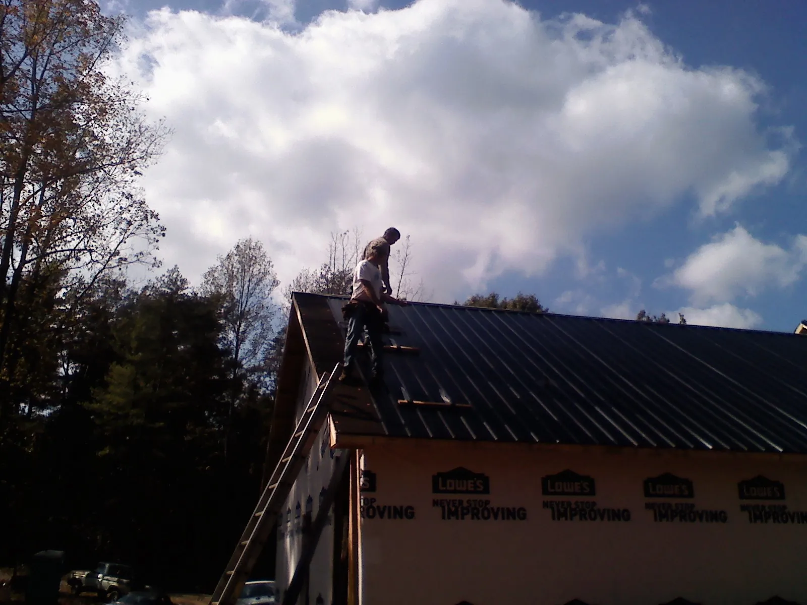 Roofer fastening dark metal panels high against a cloudy sky, from a Roof Inspection job in Dallas